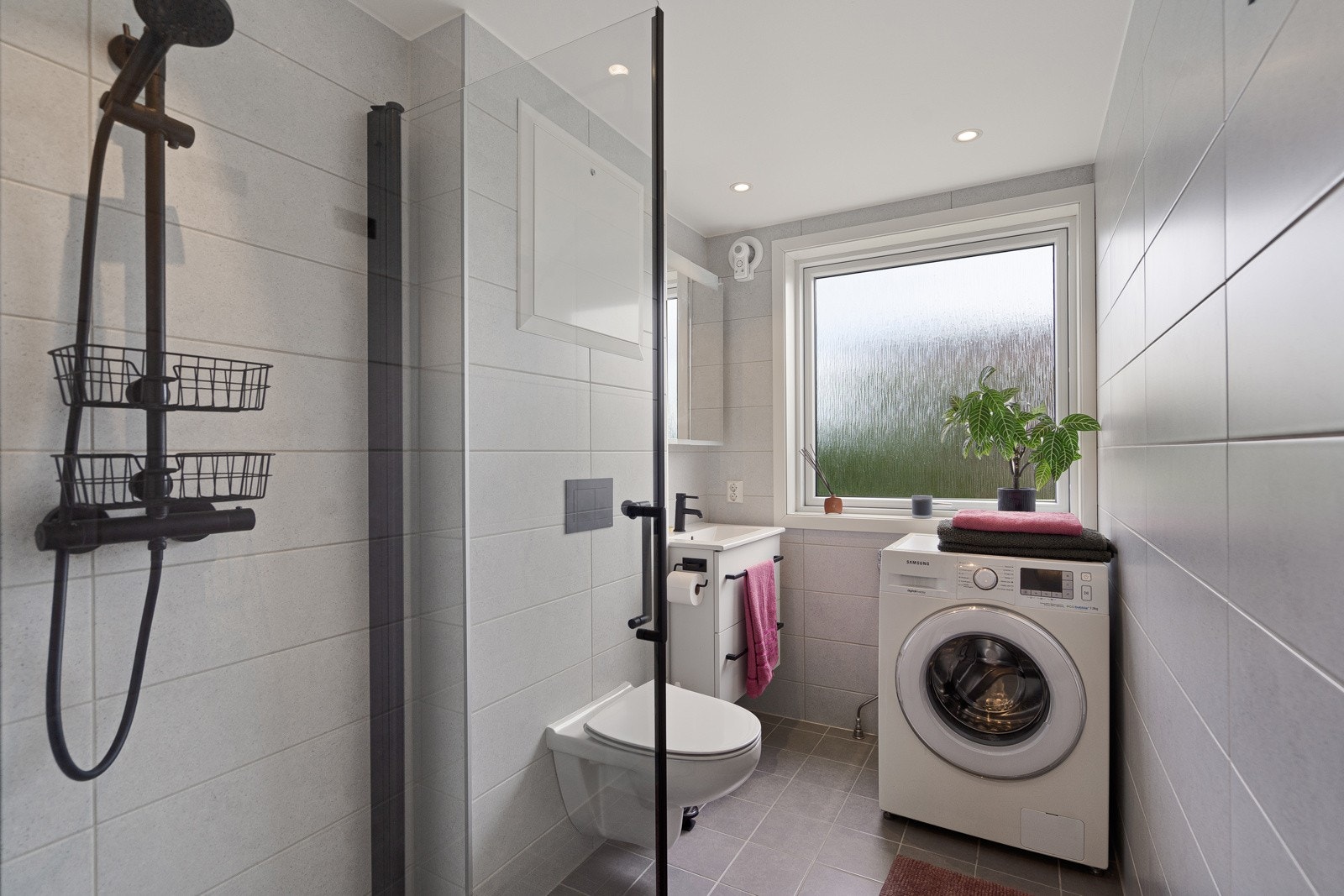 Badet ble pusset opp i 2022 og fremstår moderne og pent, med fliser på gulv og vegger, vegghengt toalett, dusjhjørne og servant med underskap. I tillegg er det opplegg for vaskemaskin og elektrisk vifte for avtrekk. Galleribilde