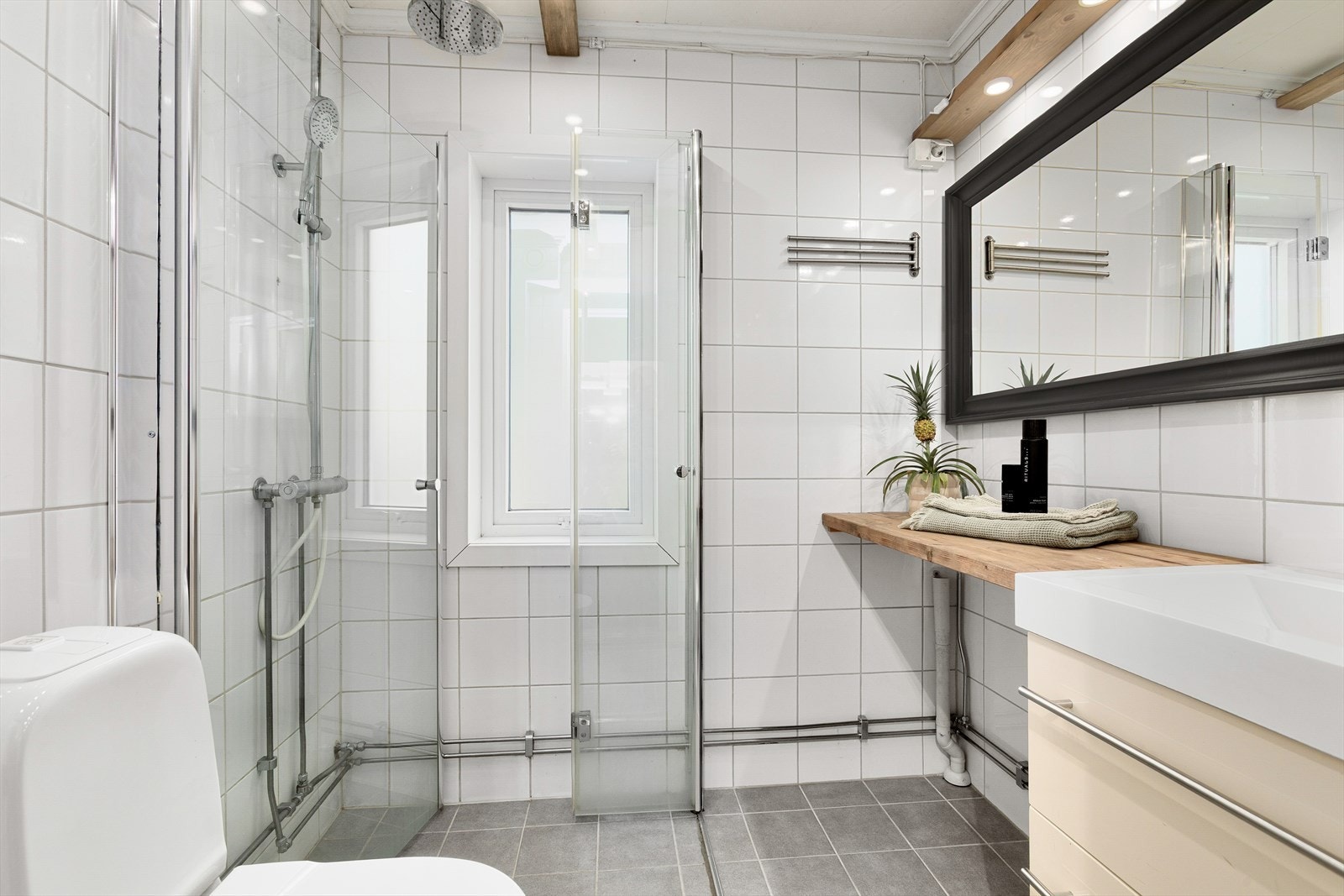 Badet er innredet med servantskap, heltre benkeplate, vegghengt speil, dusj med glassdører og gulvmontert toalett. Galleribilde