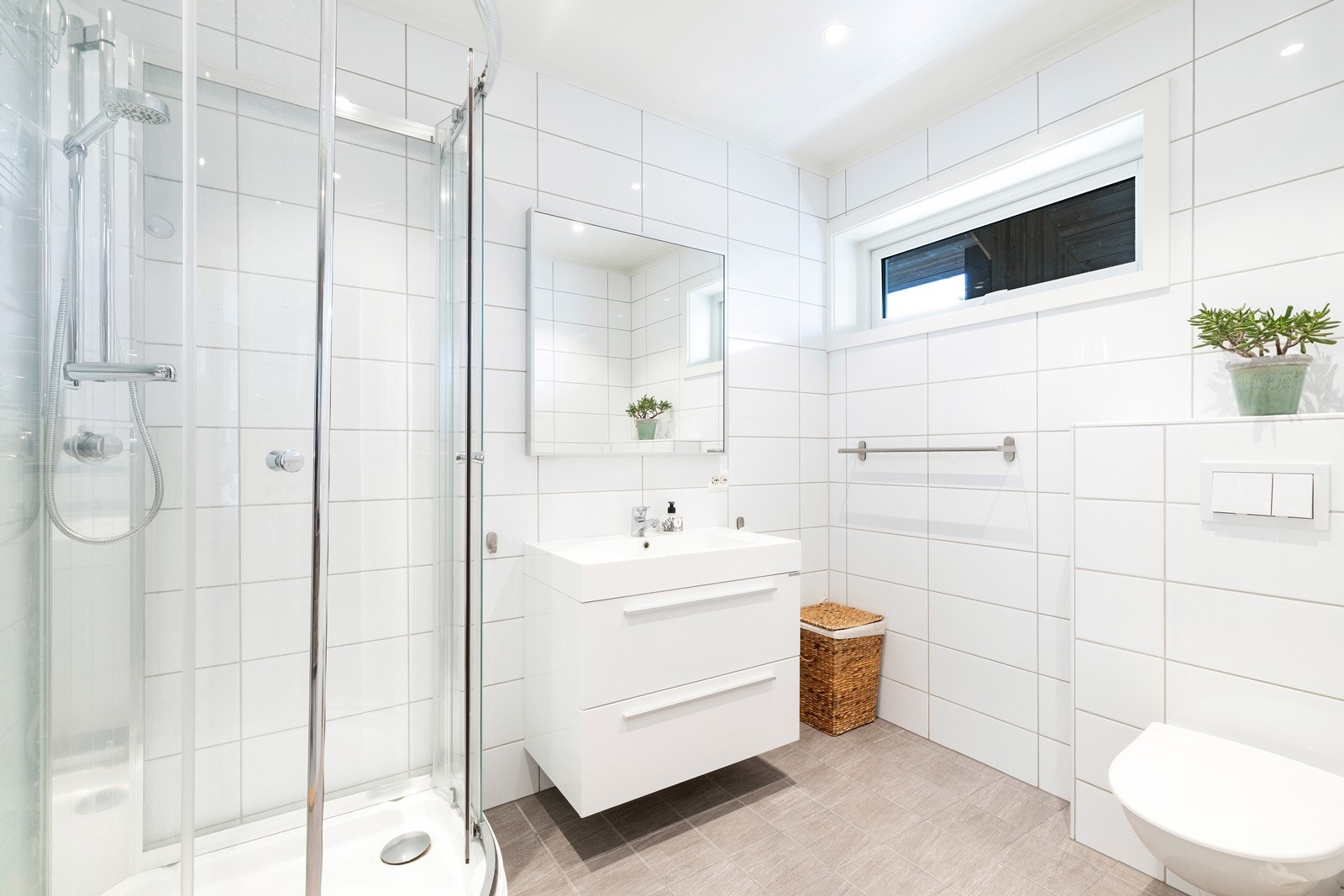 Flislagt bad med dusjkabinett, servant med underskuffer og vegghengt toalett. Galleribilde