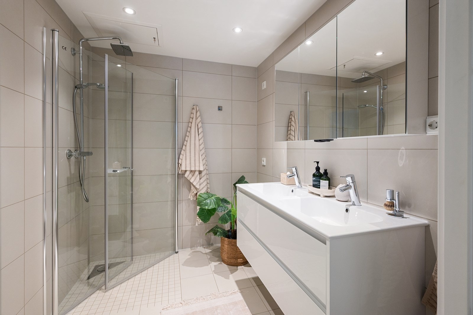 Badet er inredet med vegghengt toalett, dobbel servant på heldekkende baderomsinnredning, speilskap og dusjhjørne med glassvegger. Galleribilde