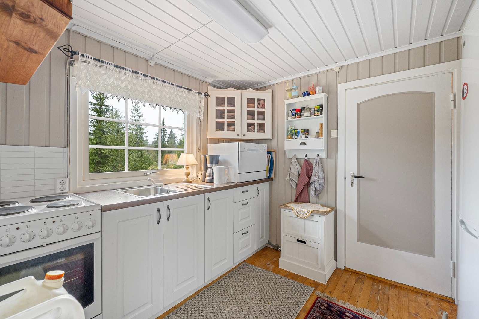 Kjøkkeninnredningen har underskap med profilerte fronter. Laminat benkeplate med nedfelt vask. Komfyr og kjøleskap er montert på kjøkken. Galleribilde