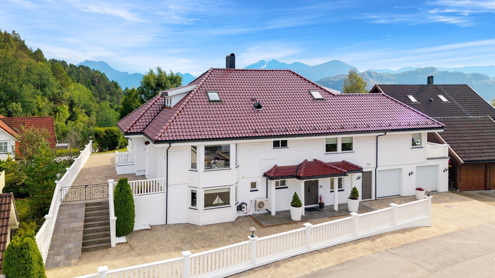 Dronebilde av fasade og adkomst mot gate. Flotte opparbeidete uteområder som er steinlagt og avgrenset med gjerde mot gate Galleribilde