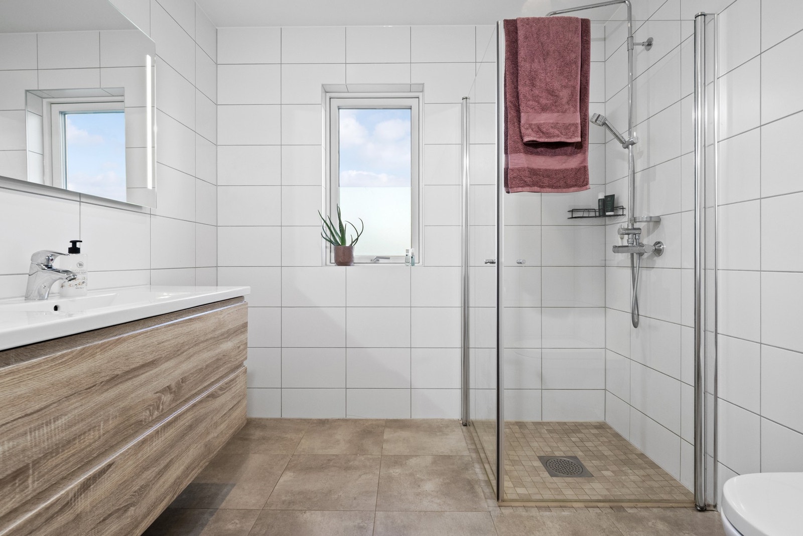 Badet oppe har et delikat uttrykk med hvite veggfliser og store, lysegrå fliser på gulvet. Galleribilde