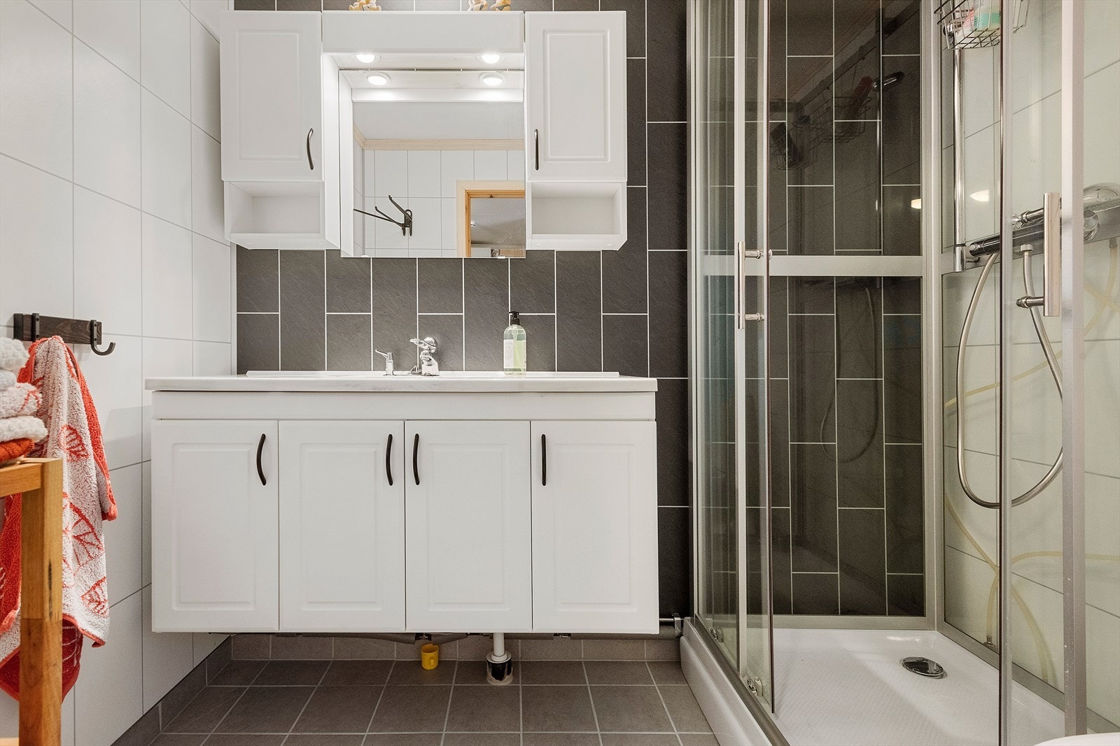 Baderommet er innredet e klassisk, tidløs stil med hvite og mørke våtromsplater på vegg og flislagt gulv med varmekabler. Galleribilde