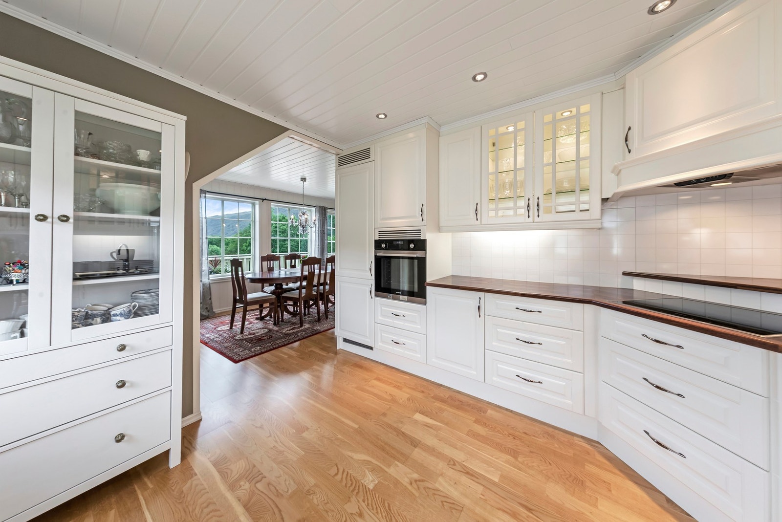 Kjøkkeninnredning med malte profilerte fronter og benkeplate i laminat. Noen overskap med glassdører Galleribilde