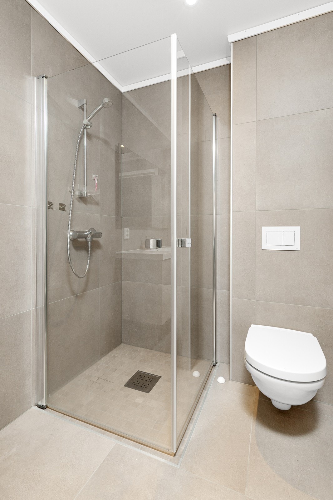 Rommet er utstyrt med moderne innredning, nedfelt servant, speil med integrert belysning, veggmontert toalett og dusjhjørne med innfellbare glassdører. Galleribilde