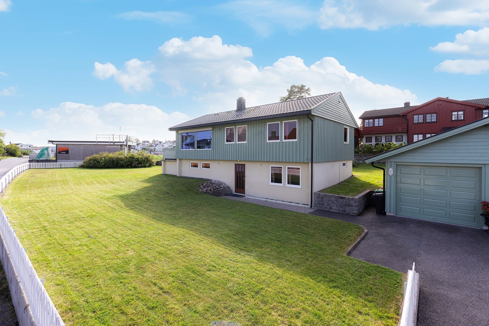 Stor og lett skrånende tomt som er pent opparbeidet med plen og prydbusker, samt asfaltert innkjørsel og flere forstøtningsmurer. Galleribilde