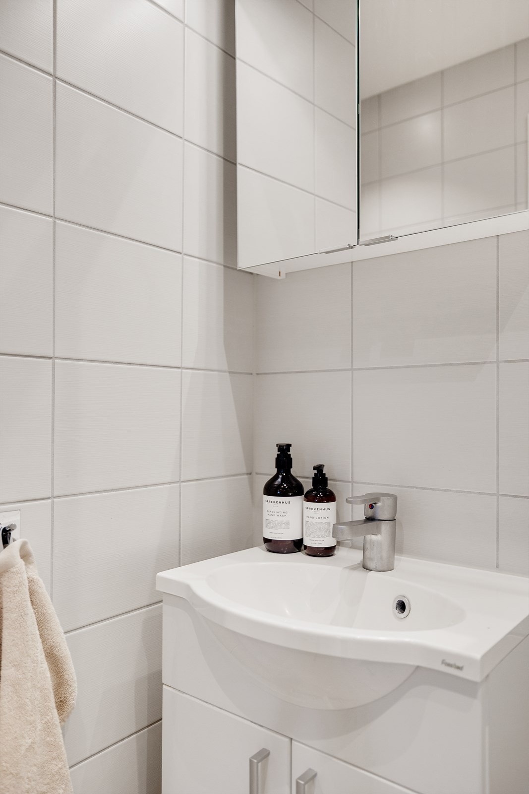 Baderomsinnredning med finerte glatte fronter og heldekkende servant samt speilskap med belysning over. Galleribilde