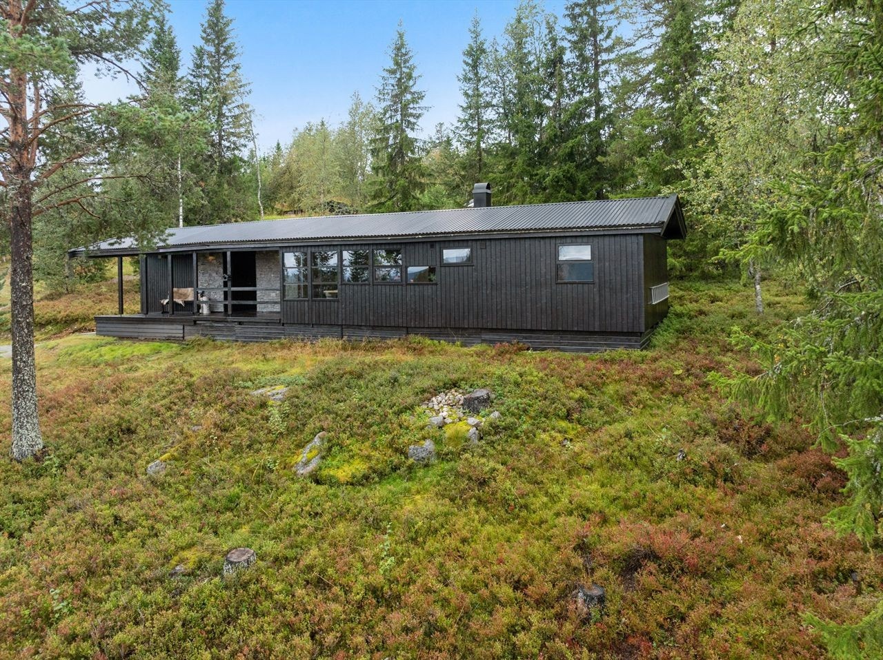 Stilren hytte med mørk kledning, harmonisk plassert i naturskjønne omgivelser. Galleribilde