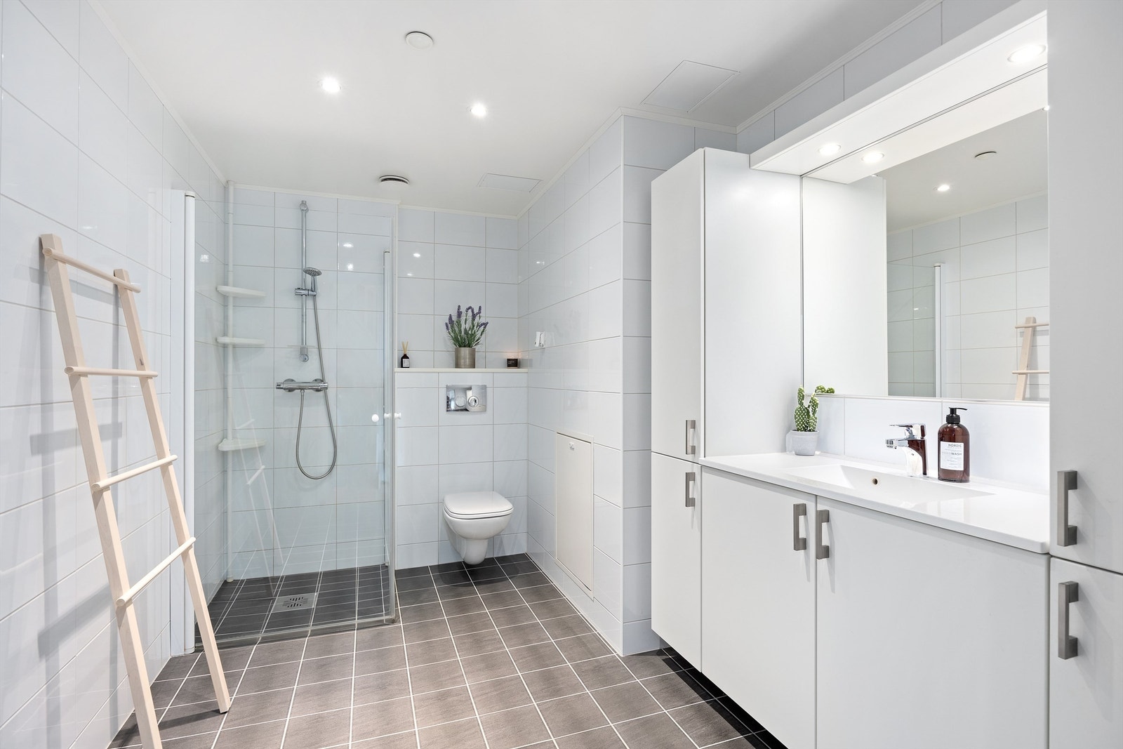 B A D E V Æ R E L S E I: Lyst og delikat badeværelse med vegghengte innfellbare dusjdører i herdet glass. Rikelig med oppbevaring i flere skap Galleribilde