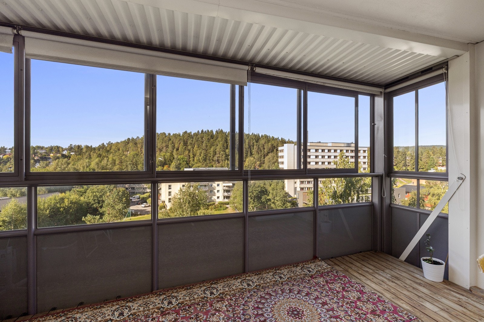 Balkongen er overbygget, har terrassebord på gulv og rekkverk med store skyvbare vinduer som kan åpnes opp. Galleribilde