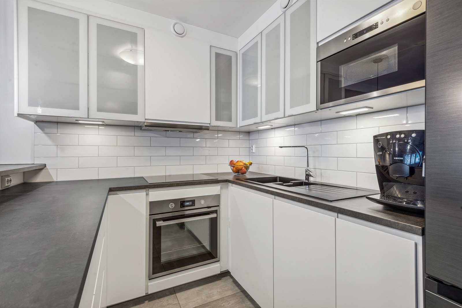 Kjøkkenet har hvite slette fronter, og integrerte hvitevarer som stekeovn, koketopp og oppvaskamskin Galleribilde