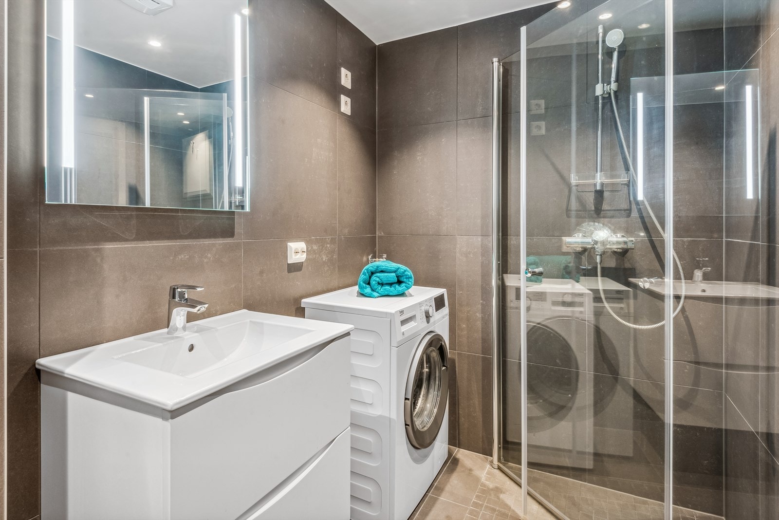 Det er flislagt, og inneholder dusjhjørne, servant med speil, vegghengt toalett og opplegg til vaskemaskin Galleribilde