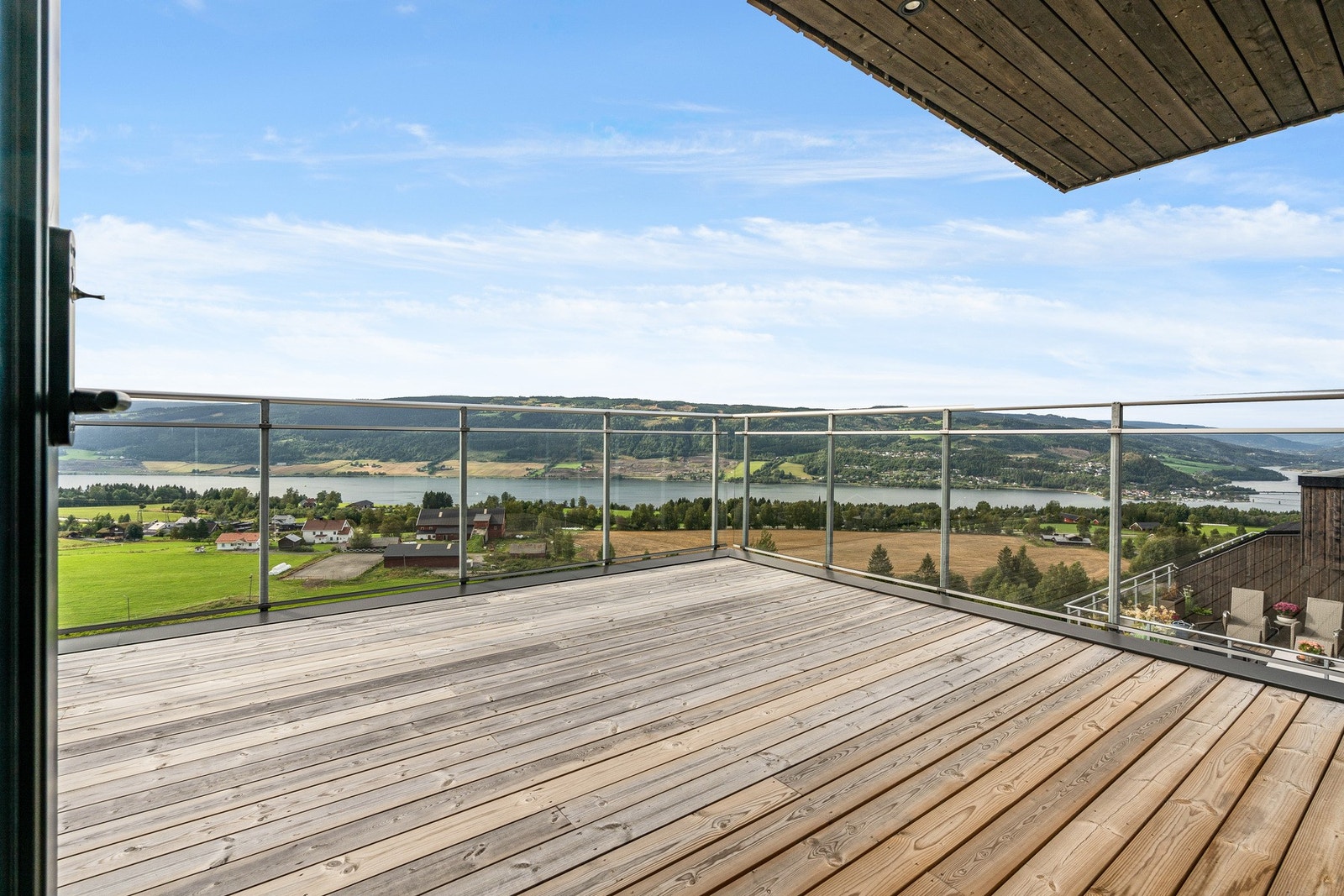 Stor og luftig terrasse med glassrekkverk og dels overbygget. Galleribilde