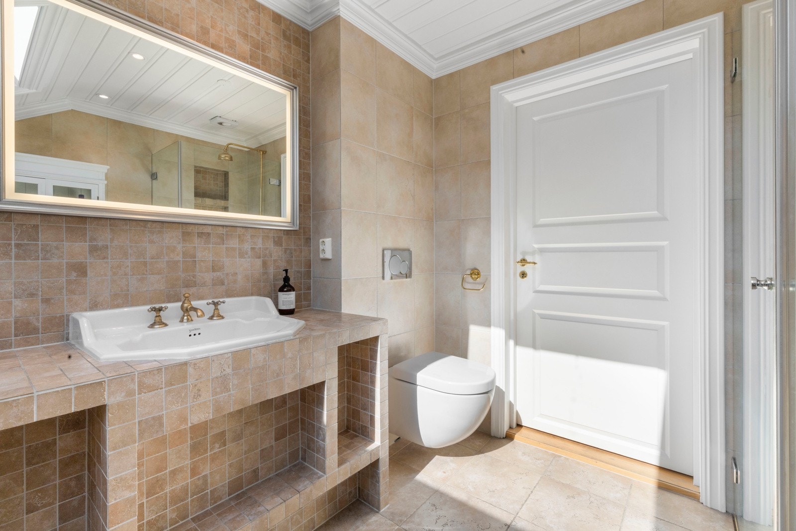 Her er det servant med flislagte overflater, frittstående badekar, vegghengt toalett, samt en dusjsone.