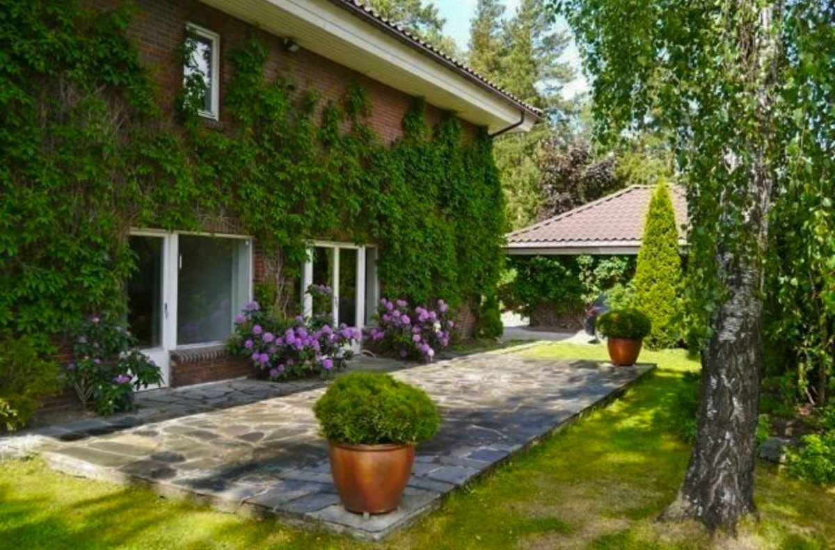 Privat bilde. Inngangspartiet ønsker deg velkommen med en hyggelig, steinlagt platting og frodige rhododendronbusker.