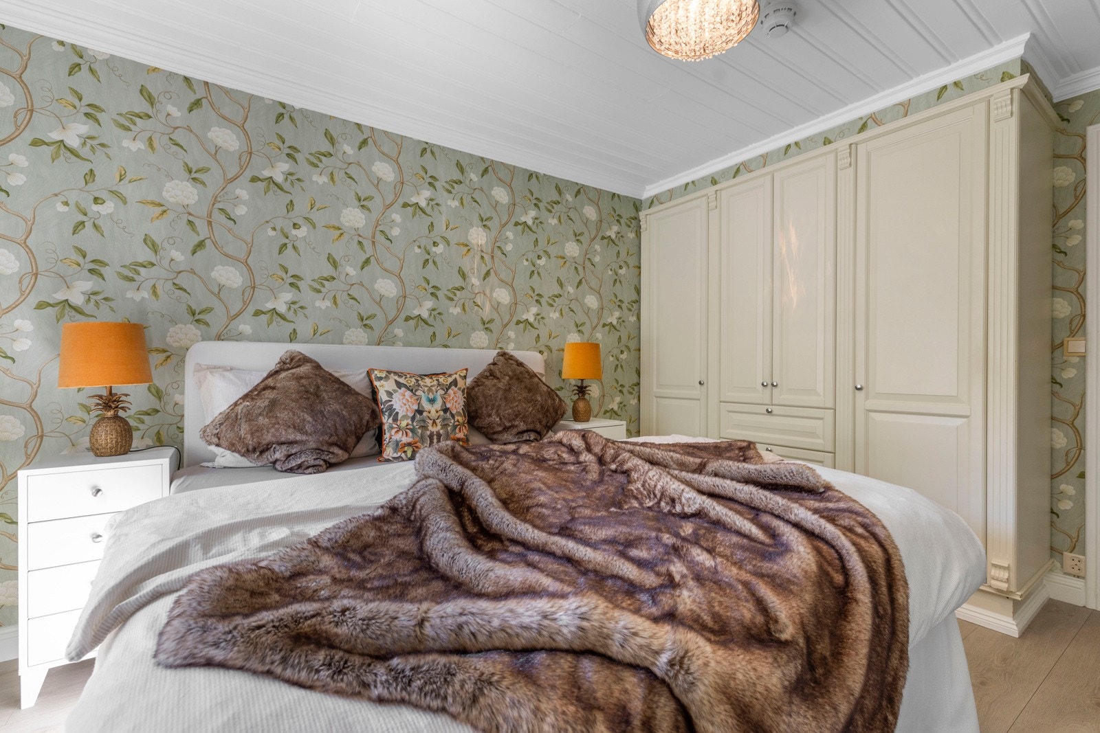 Soverommet fremstår stilfullt med delikat veggtapet i behagelige fargetoner og et lekkert blomstermotiv, kombinert med et praktisk, integrert garderobeskap.