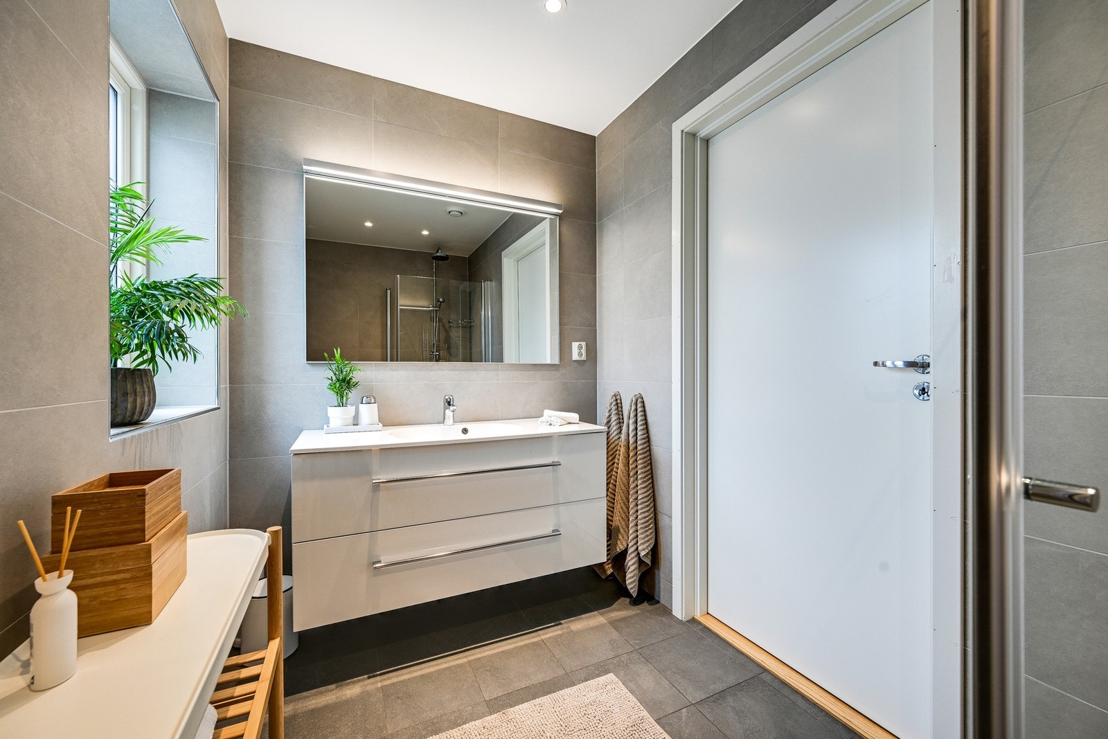 Baderom nr. 2 er i første etasje med flis på gulv og vegger. Rommet er godt belyst med spotter, og inneholder servant i innredning med skuffer og speil. Galleribilde