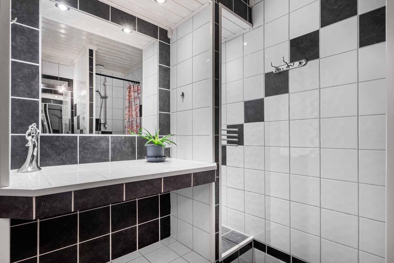 Badet har flislagte gulv og vegger, varmekabler og plassbygd benk og hylle med speil og downlights. Galleribilde