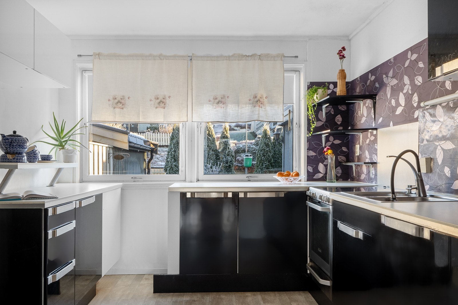 Kjøkkeninnredningen består av over- og underskap med sorte, slette fronter og benkeplate i laminat. To store vinduer gir lys og luftemulighet. Galleribilde