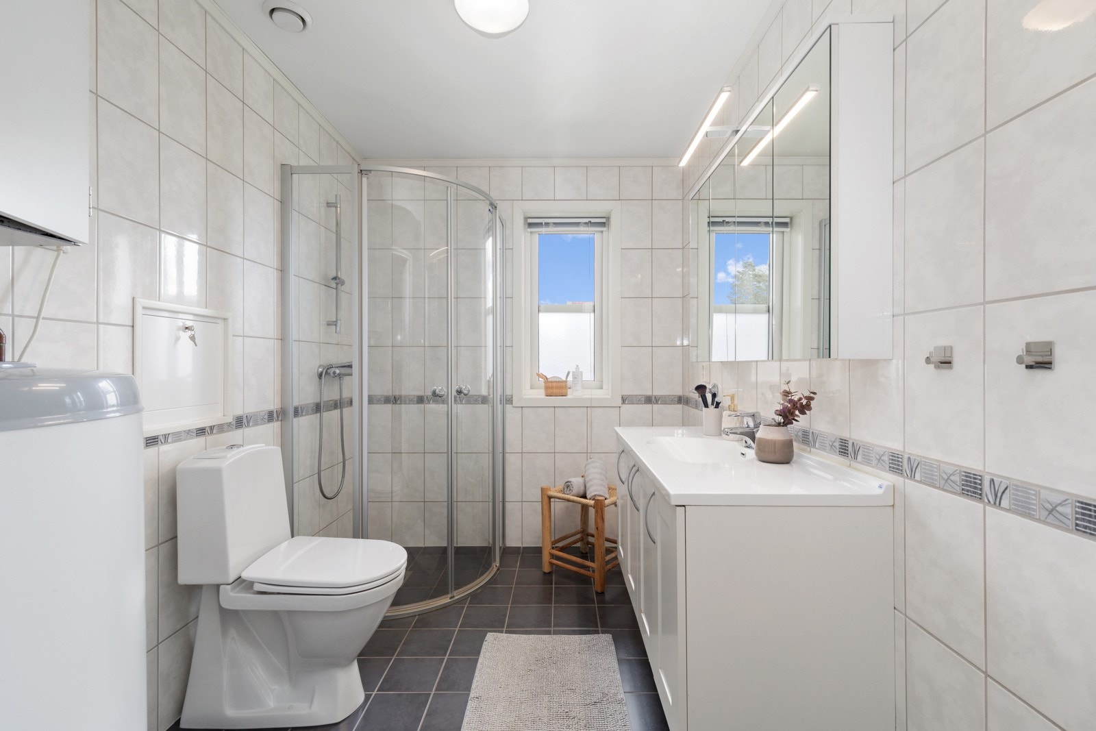 Badet har fliser på gulv og vegg. Her er det montert innredning med servant, wc og dusjkhjørne. Avsatt plass til vaskesøyle. Galleribilde