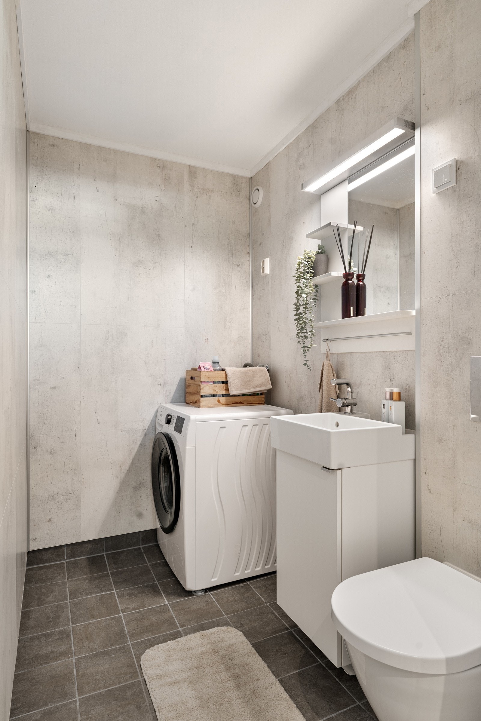 Vegg i vegg med entréen har man et pent og praktisk vaskerom fra 2020. Innredet med vegghengt toalett, servant i en lys innredning samt plass for vaskemaskin og tørketrommel. Galleribilde