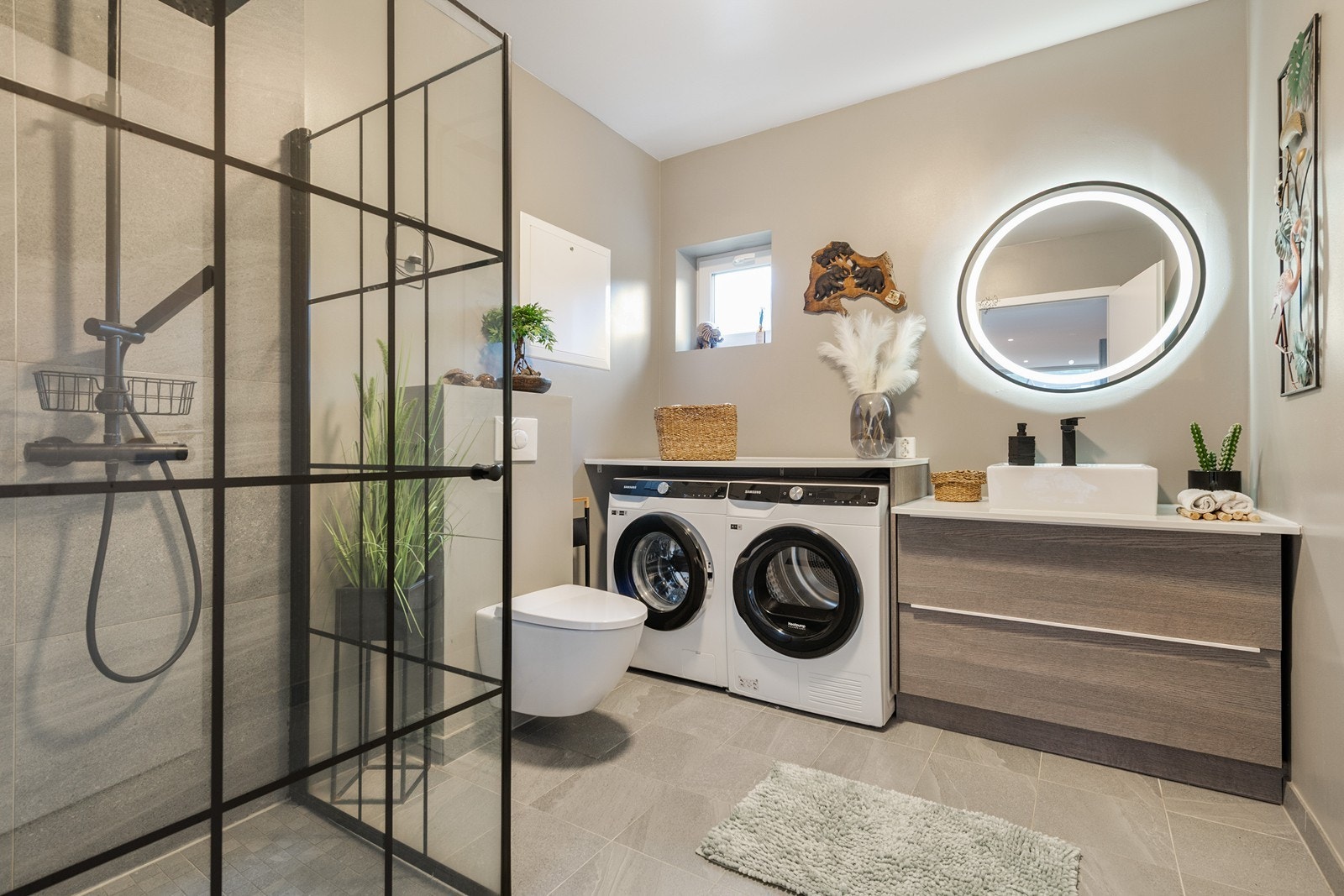 Badet i 1 etg fremstår moderne og stilrent. Badet har også praktisk opplegg for vaskemaskin og tørketrommel, plassert i en egen nisje med integrert benk. Galleribilde