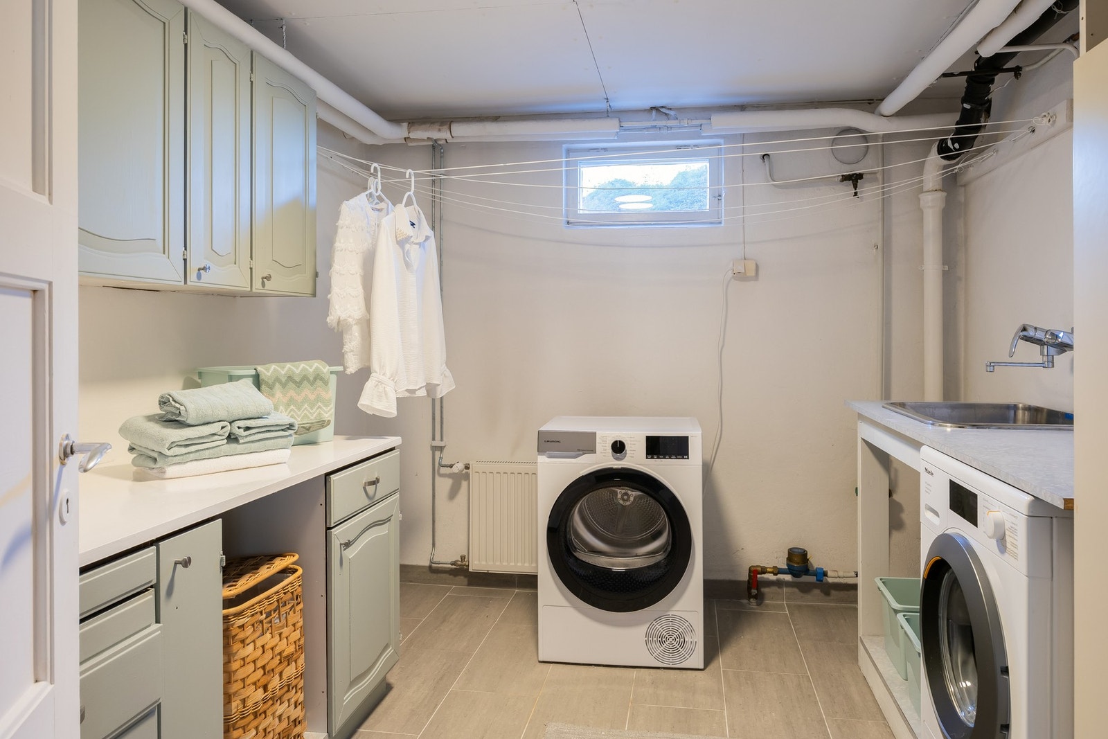 Separat vaskerom på 9m² i kjeller. Rommet har fliser på gulv. Her er flere skap og benkeplate, opplegg for vaskemaskin/tørketrommel og utslagsvask.