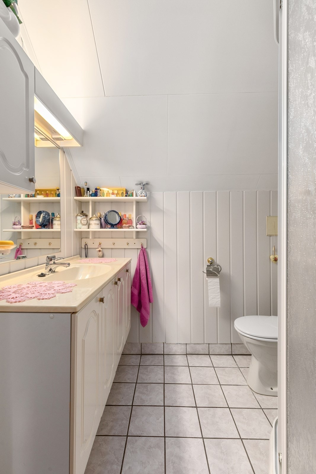 Baderom med fliser på golv og panel på veggar. Baderommet er utstyrt med toalett, servant med innredning og dusjhjørne. Galleribilde