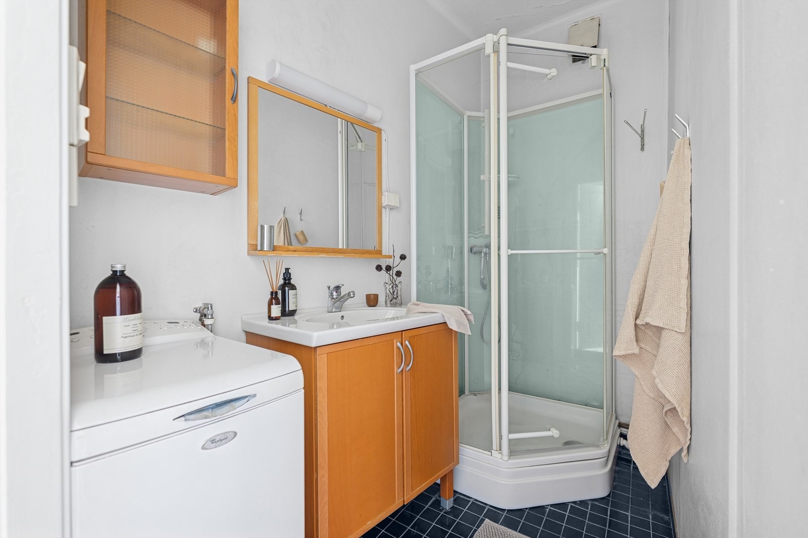 Eldre baderom med servantinnredning med speil, opplegg for vaskemaskin og dusjkabinett. Det er lagt opp rørgjennomføring via kjøkken. Rommet har ikke sluk i gulvet. Galleribilde