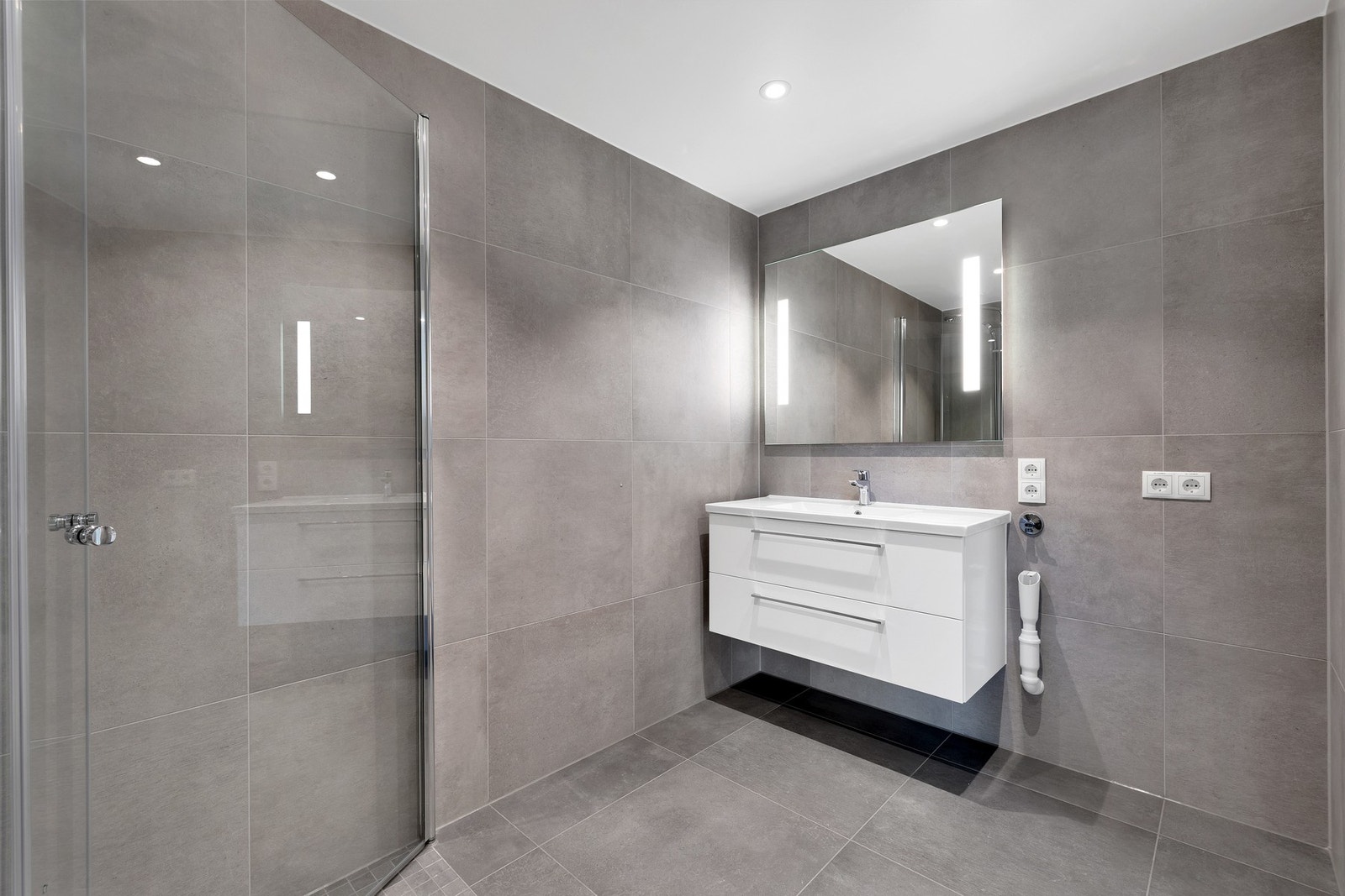 Pent og elegant bad med fliser på gulv og vegger. Innfellbare dusjdører. Opplegg for vaskemaskin. Galleribilde