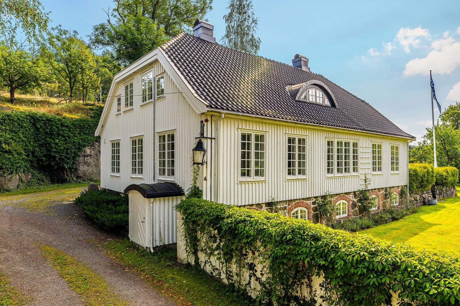 Uteområdene er frodige og innbydende med høye trær, lubne busker og klatreplanter som slynger seg opp husveggen. Galleribilde