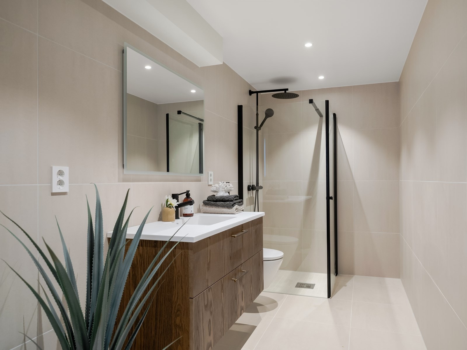 Badet i underetasjen er i samme stil som hovedbadet med flislagte overflater, gulvvarme og downlights i tak. Servantseksjon i treverk med stort speil over, vegghengt toalett og dusjhjørne med regnfallsdusj. Her er det også opplegg til vaskemaskin. Galleribilde