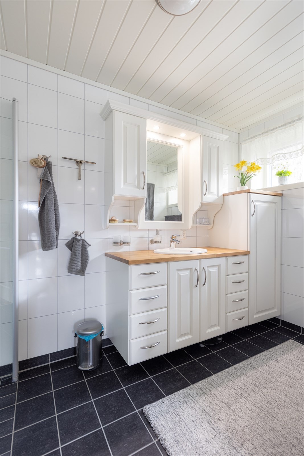 Badet er innredet med dusjhjørne, vegghengt toalett og servantinnredning med underskap, skuffer, sideskap, overskap og speil. Galleribilde