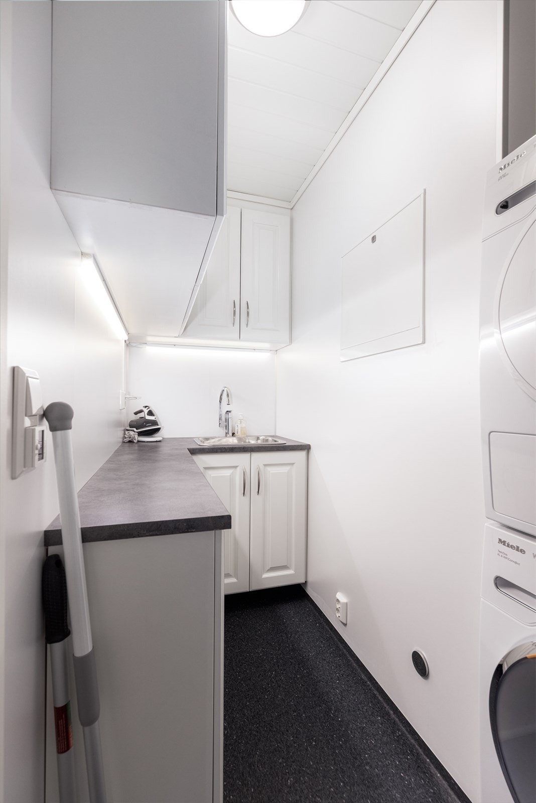 Praktisk vaskerom med belegg på gulvet med gulvvarme, og plater på vegg. Rommet er innredet med skapinnredning med god plass for oppbevaring av vaskemidler etc. Galleribilde