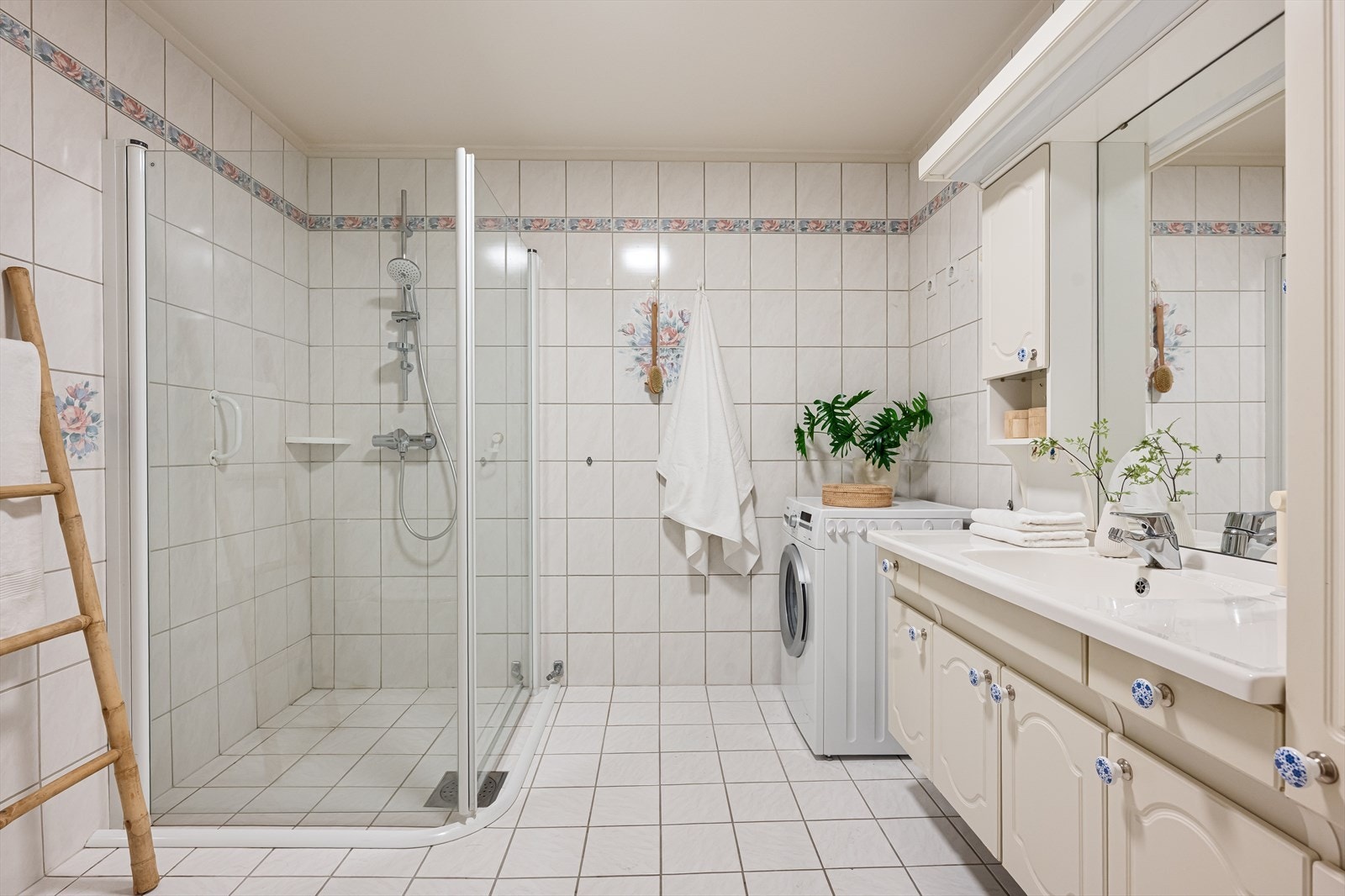 Romslig flislagt bad med dusjhjørne og opplegg for vaskemaskin. Galleribilde
