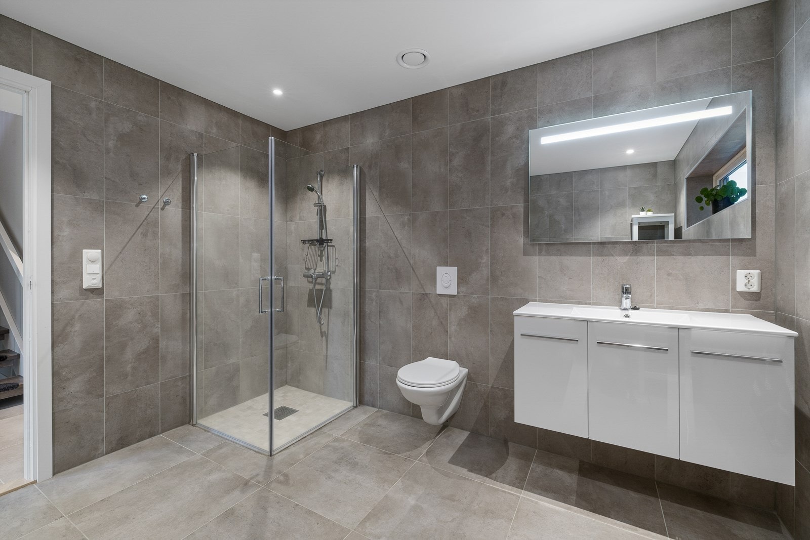 Lekkert fliselagt bad med dusjnisje, vegghengt wc, servantskap og speil. Galleribilde