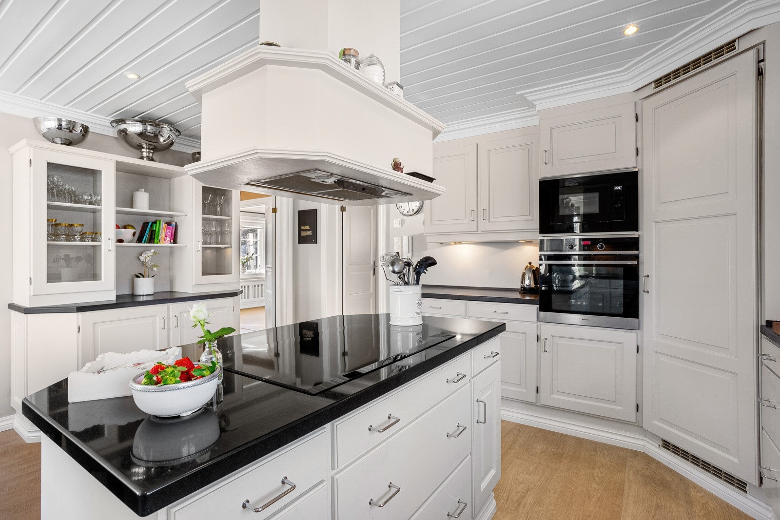 Kjøkkenet har bl.a. malte profilerte flater. Innredningen dekker flere vegger og inkluderer både overskap og kjøkkenøy. Integrerte hvitevarer, inkludert oppvaskmaskin fra Miele, stekeovn fra Gram, kjølehjørne fra Norcool og induksjonsplatetopp fra Witt Galleribilde