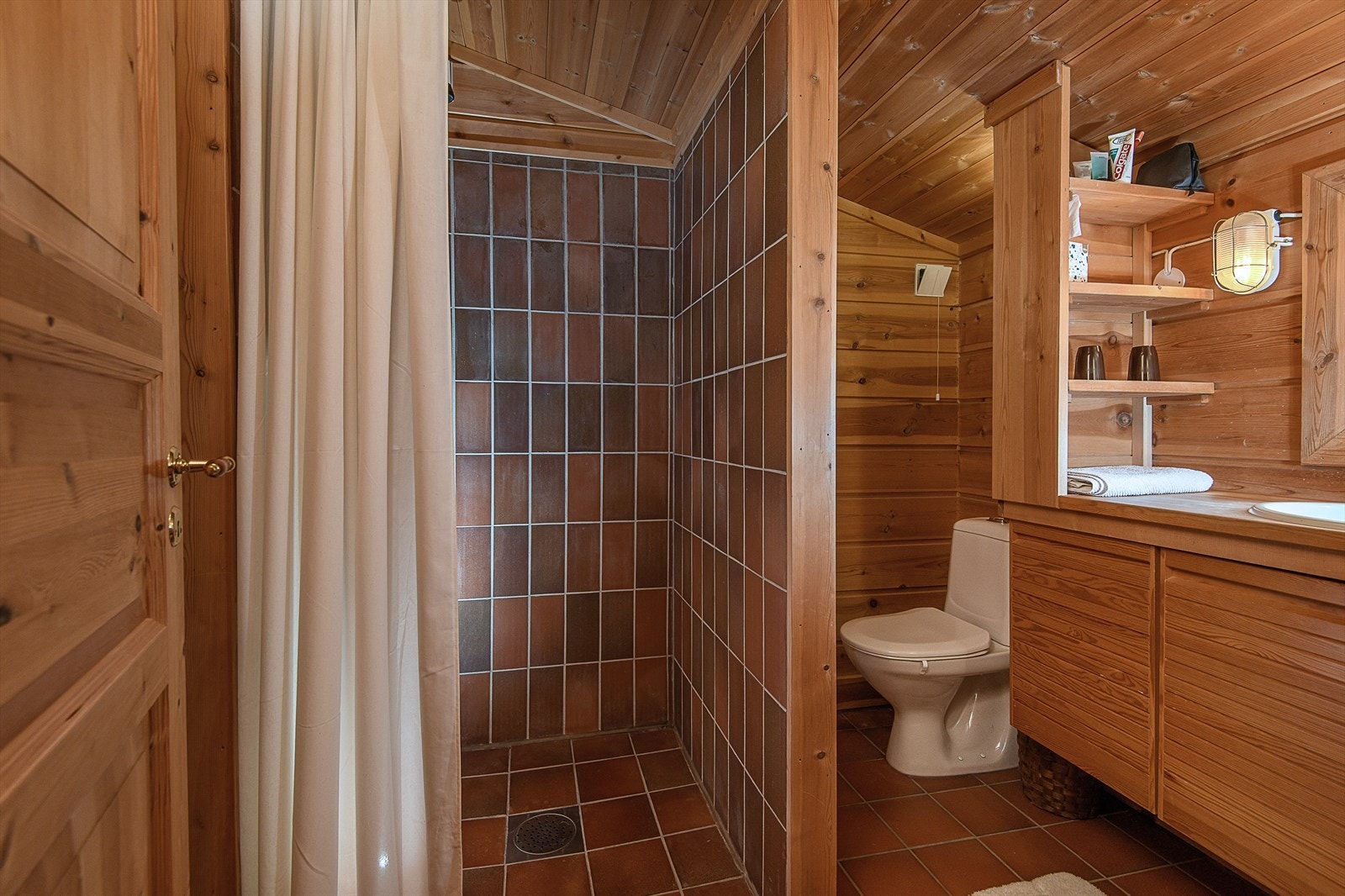 Badet i har flislagt gulv og fliser i dusjsonen, mens øvrige vegger er kledd med panel og tømmer. Galleribilde