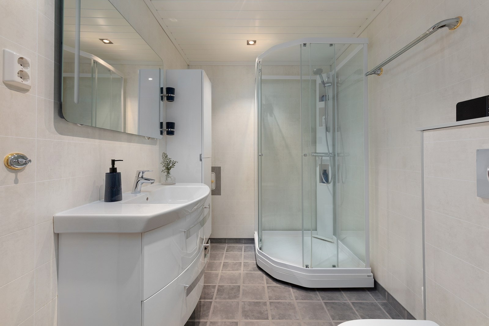 Bad med fliser på golv og plater på veggar. Badet er utstyrt med varmekabler i golv, nyare dusjkabinett, toalett og stor innreiing med nedfelt servant. Galleribilde