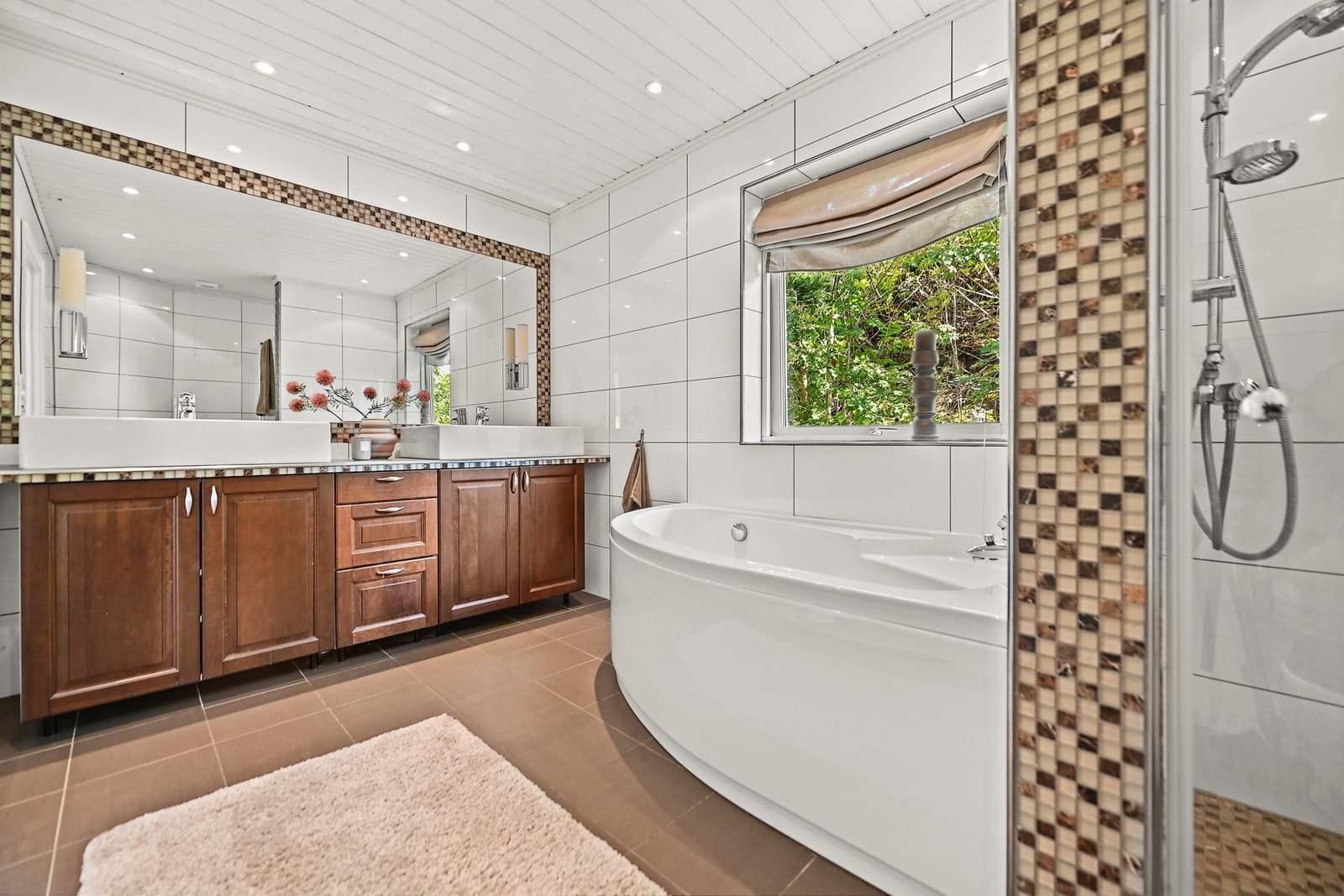 Badet er innredet med både badekar og dusjnisje, vegghengt toalett, servantskap med flislagt benk og to påliggende vasker, samt et speil integrert i veggen. Galleribilde