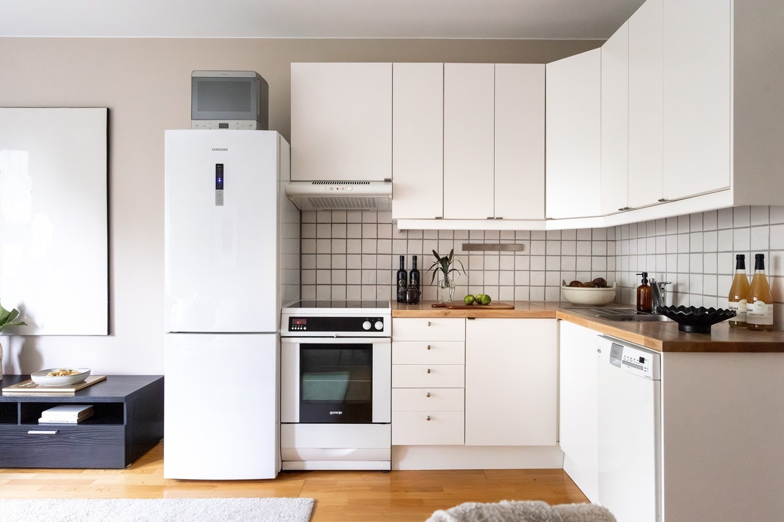 Stilrent kjøkken hvor kjøkkeninnredningen består av hvite, glatte fronter og benkeplate av heltre med nedfelt vaskekum og fliser over benkeplaten. Galleribilde