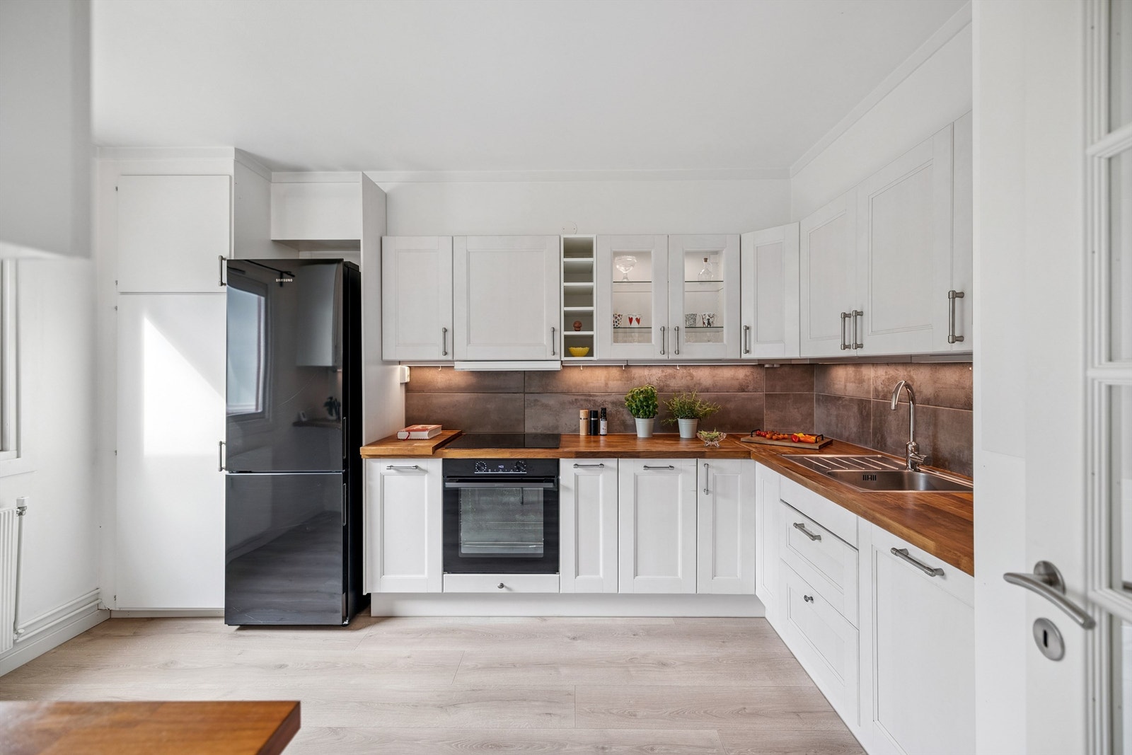 L-formet kjøkkeninnredning med malte fronter og fliser over benken. Galleribilde