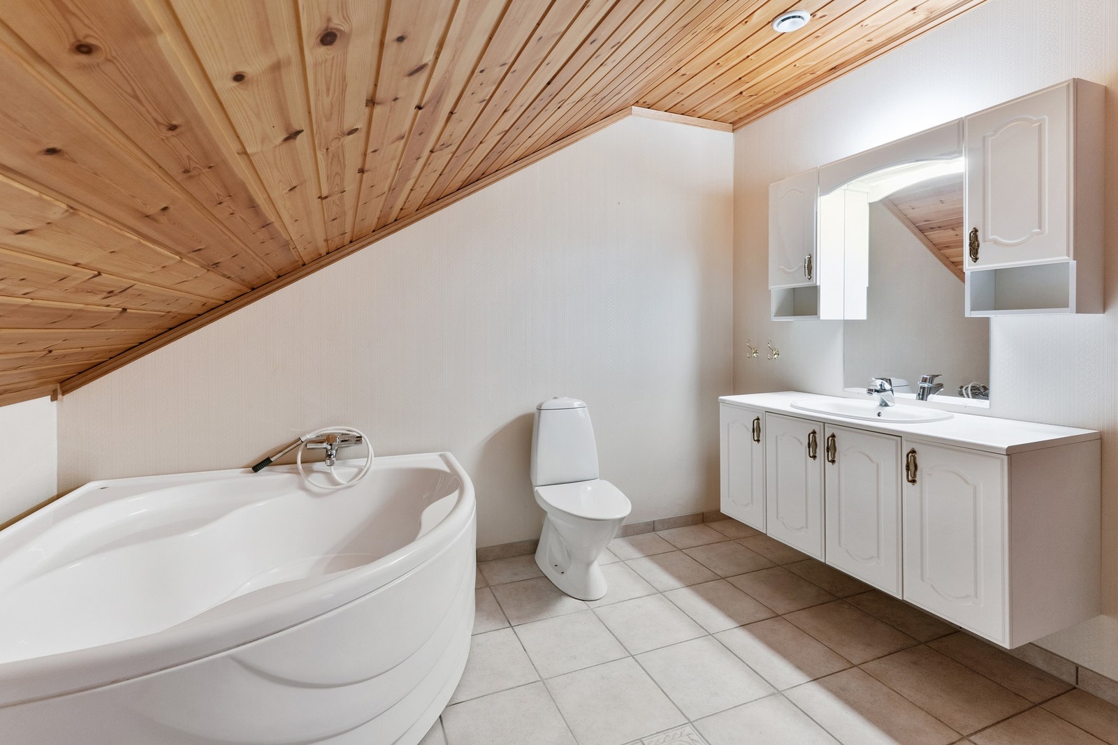 Bad på loft med baderomsinnredning, toalett og hjørnebadekar. Galleribilde