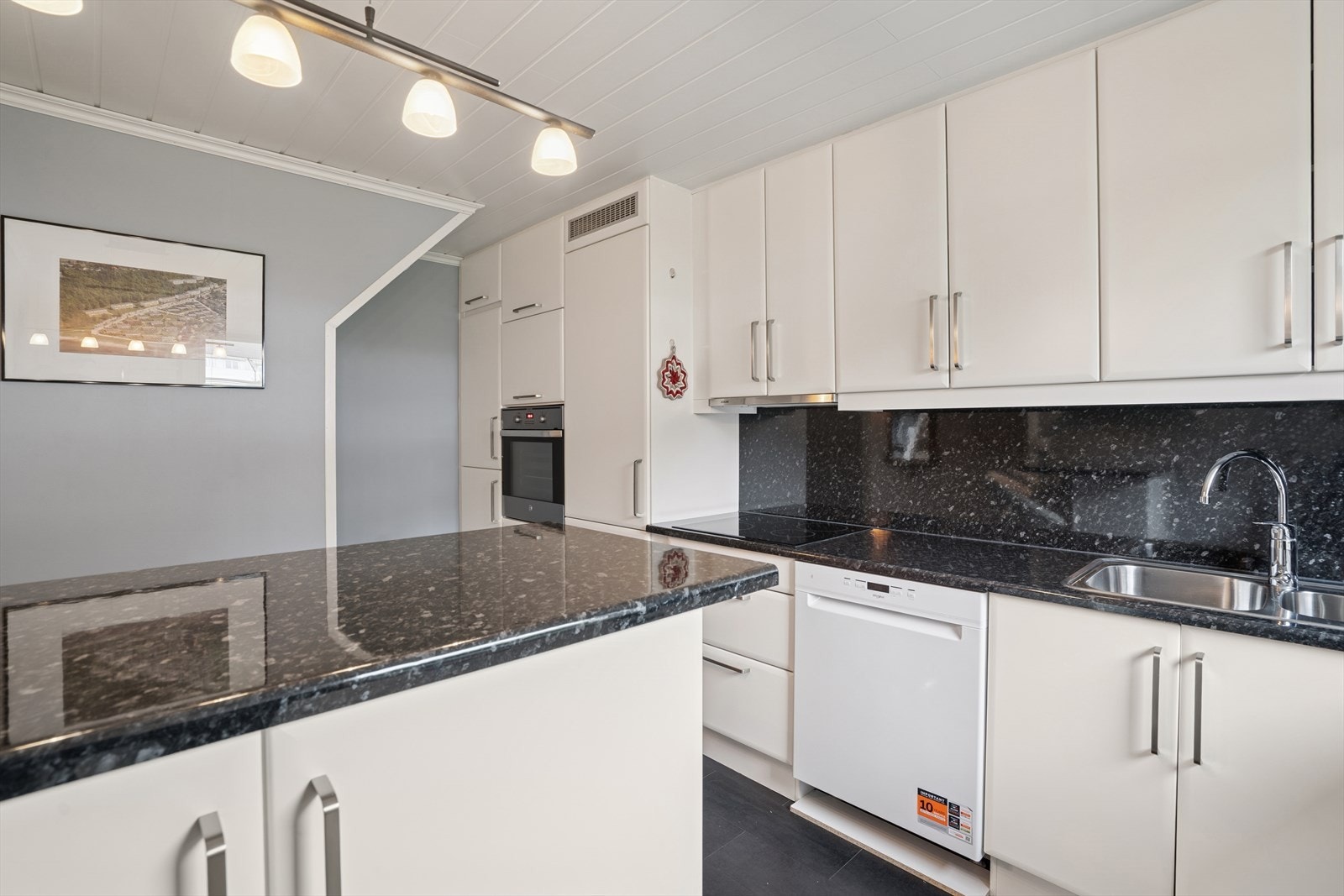 Kjøkkenet har et tidløst preg, med innredning fra 2002 som fortsatt føles aktuelt. De hvite, slette frontene gir et lyst og ryddig uttrykk, mens de sorte laminat benkeplatene tilfører en fin kontrast. Galleribilde