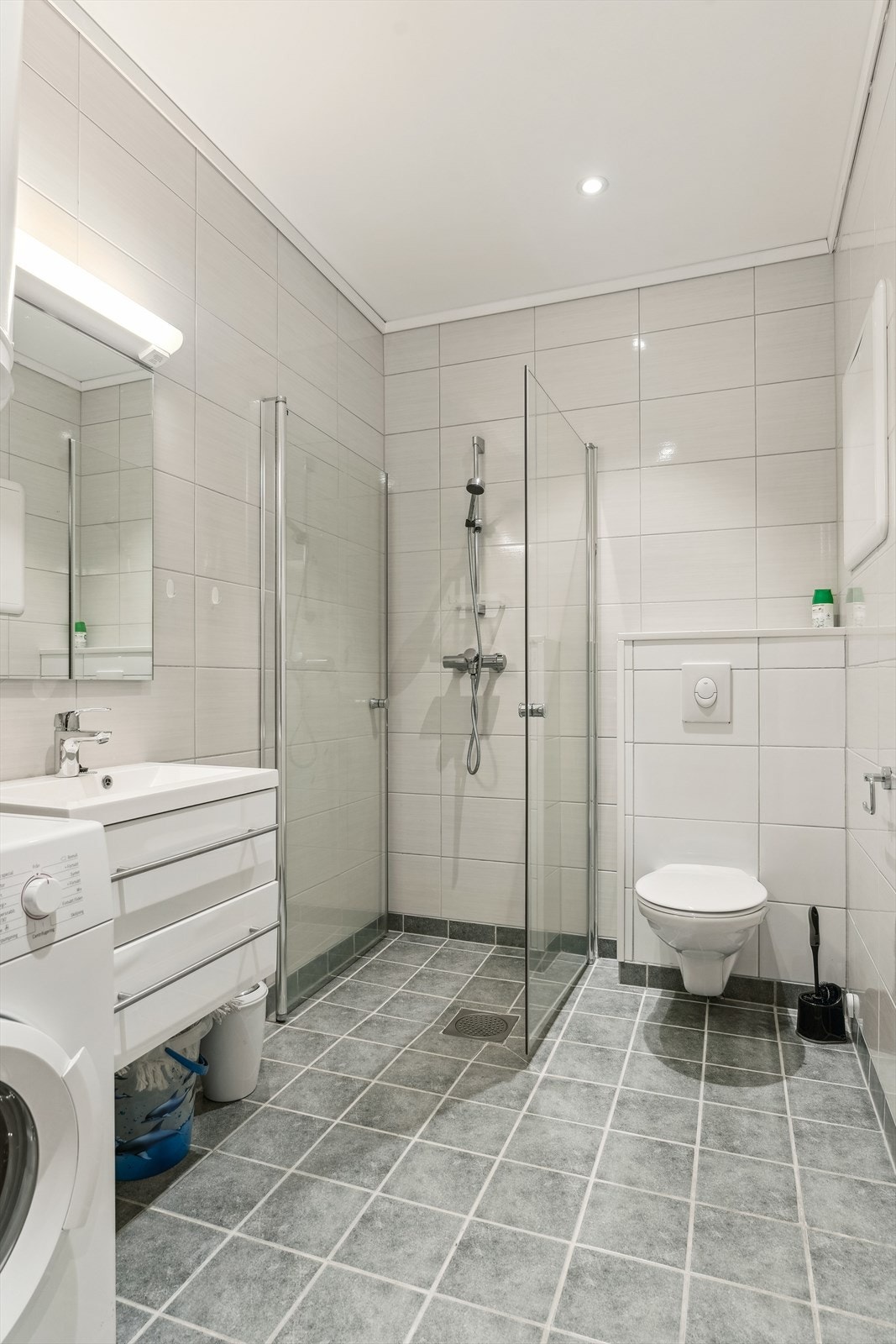 Det er dusj på golv med dusjveggar, vegghengt toalett, skuffeinnreiing med heilstøypt servant og opplegg for vaskemaskin i rommet. Galleribilde