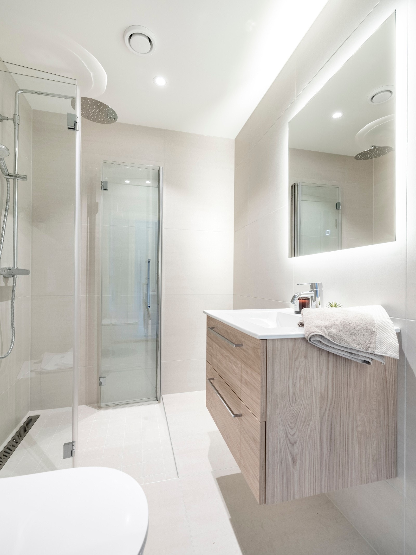 Badet er innredet med servantinnredning, speil på vegg over servant, vegghengt toalett dusjhjørne med svingbare glassdører. Galleribilde