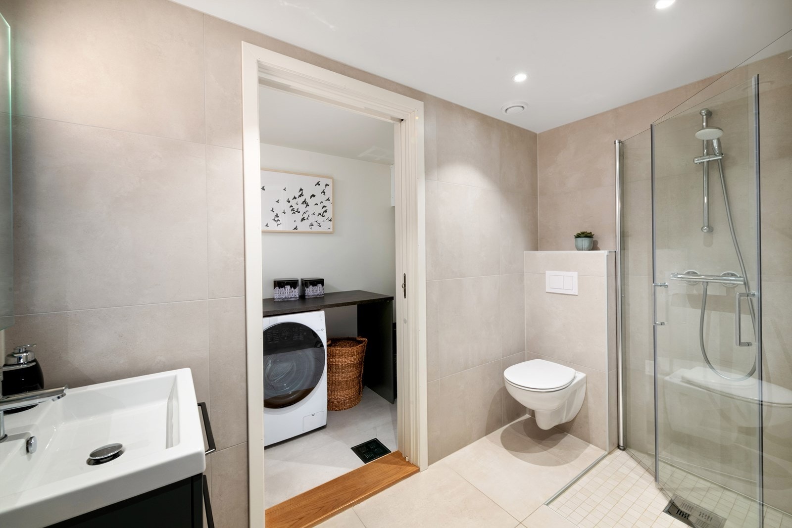 Moderne flislagt bade med varmekabler i gulv og downlights i himling. Innredet med vegghengt toalett, servantinnredning med servant, speil med integrert belysning, ettgreps blandebatteri og dusjhjørne med glassdører og dusjarmatur. Galleribilde