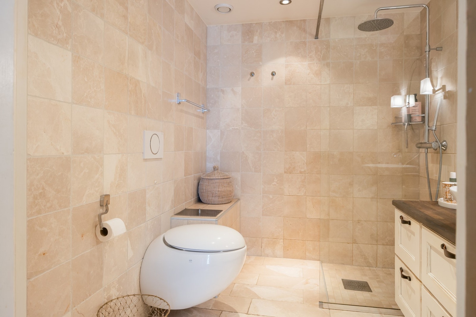 Badet er på 4,5m² og har flislagte vegger og gulv av marmor. Marmorflisen gir et moderne og elegant bad med et vegghengt toalett, dusjhjørne og baderomsinnredning.