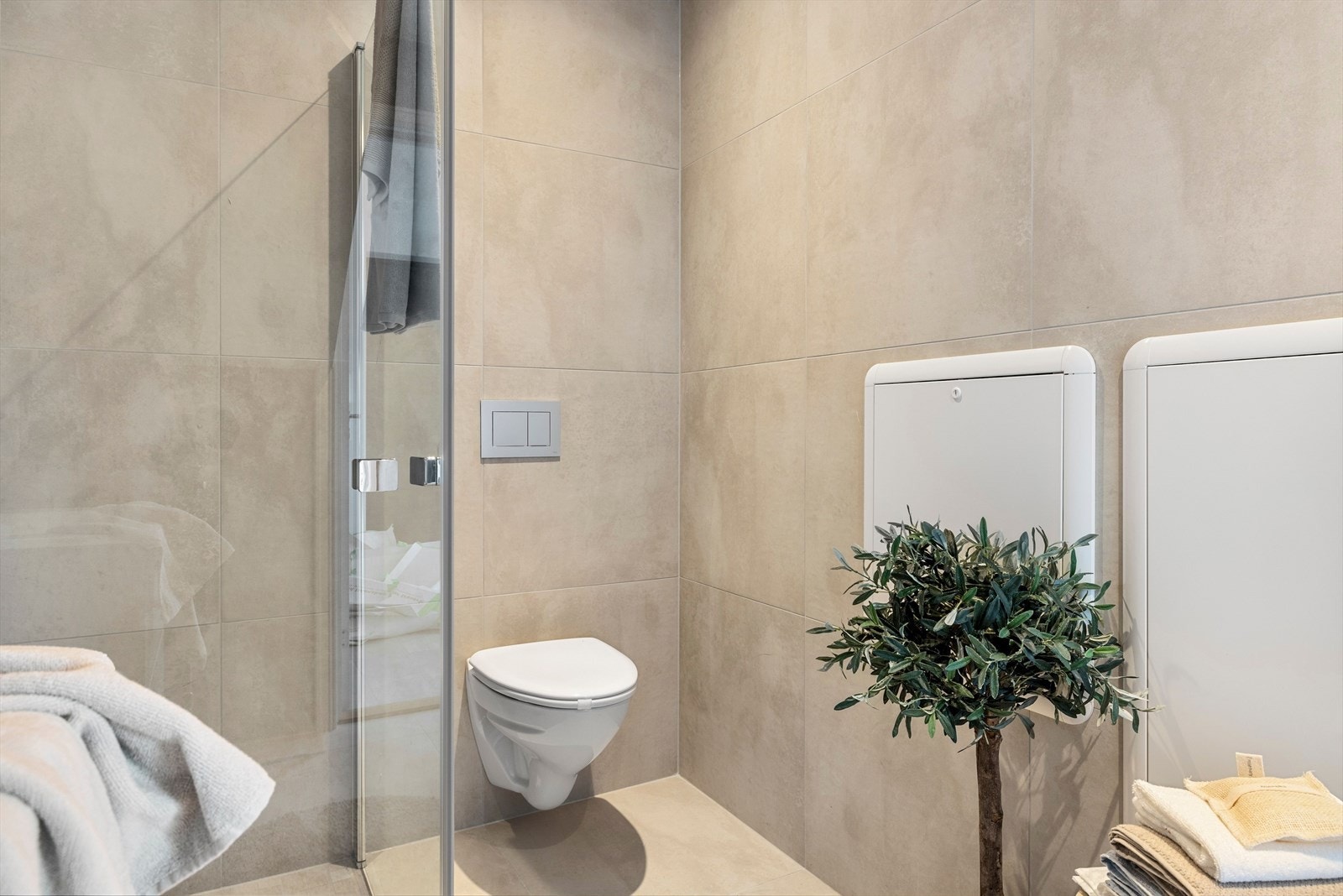 Badet har veggmontert toalett og dusjhjørne med innfellbare dusjdører og vegghengt dusjbatteri Galleribilde